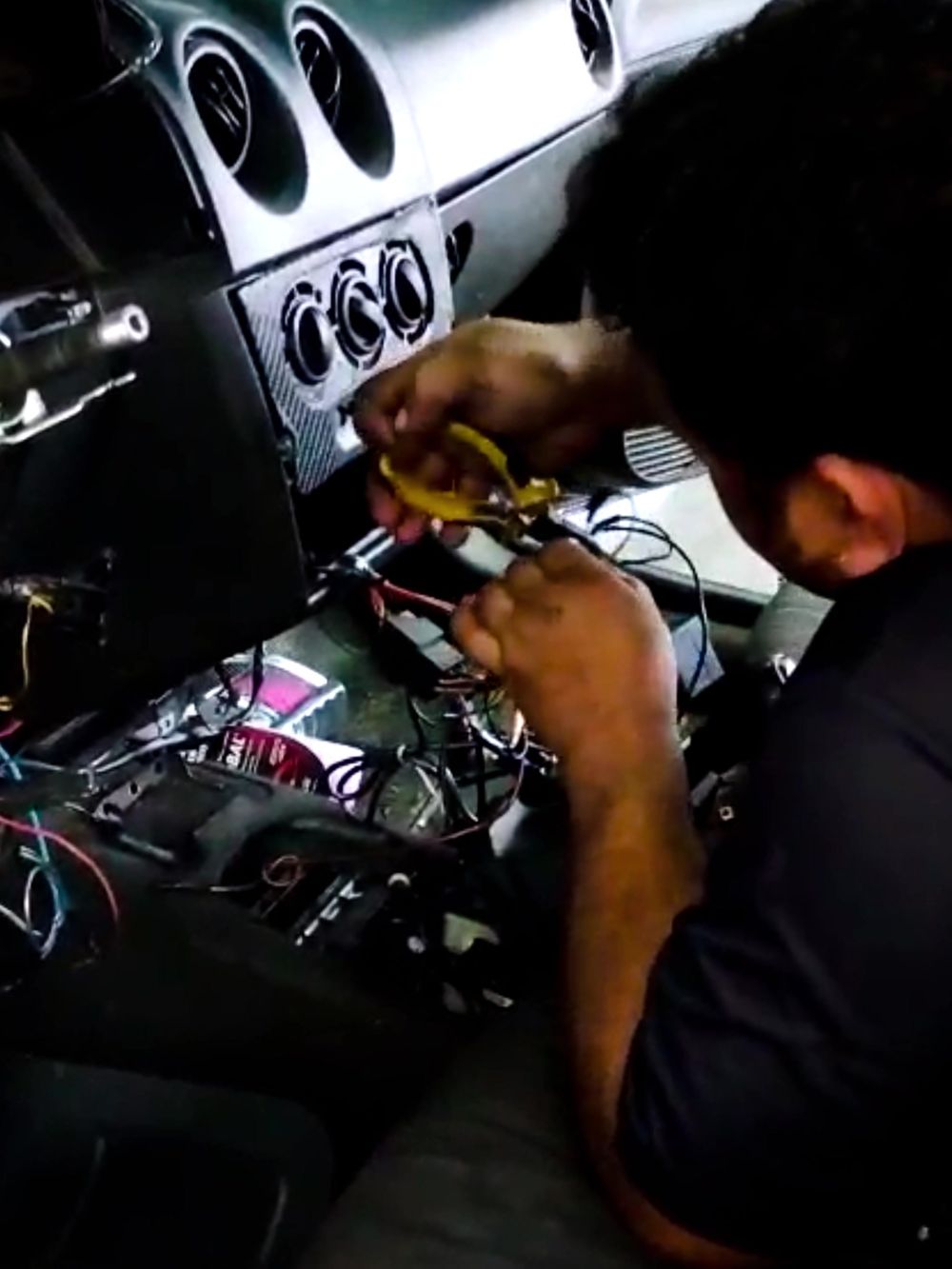 Profissional trabalhando atrás do painel do veículo, com o console removido e o chicote elétrico exposto